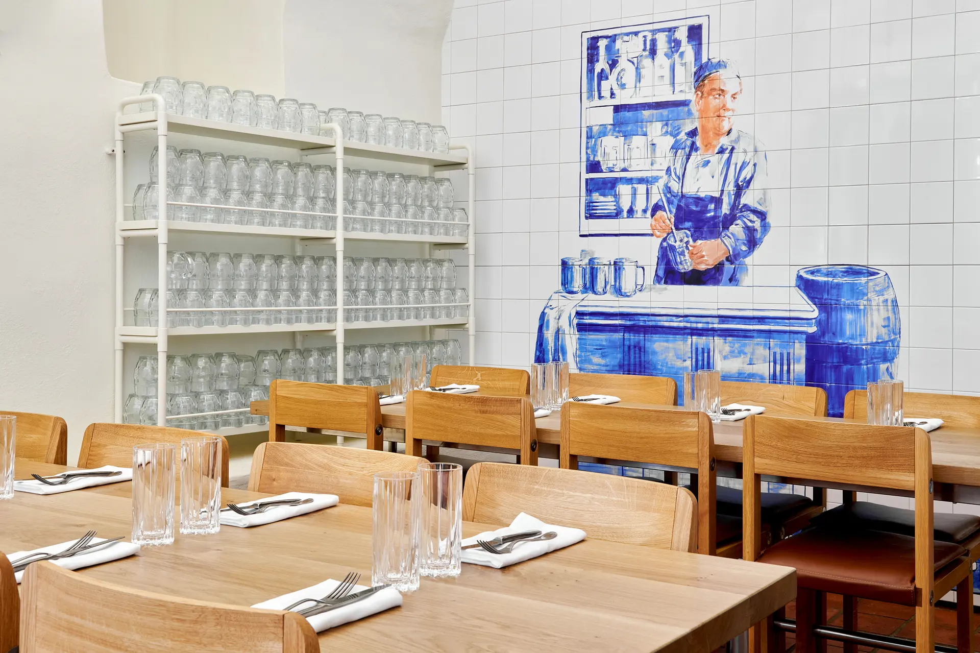 Restaurant interior with wooden tables, glassware, and a blue wall mural.